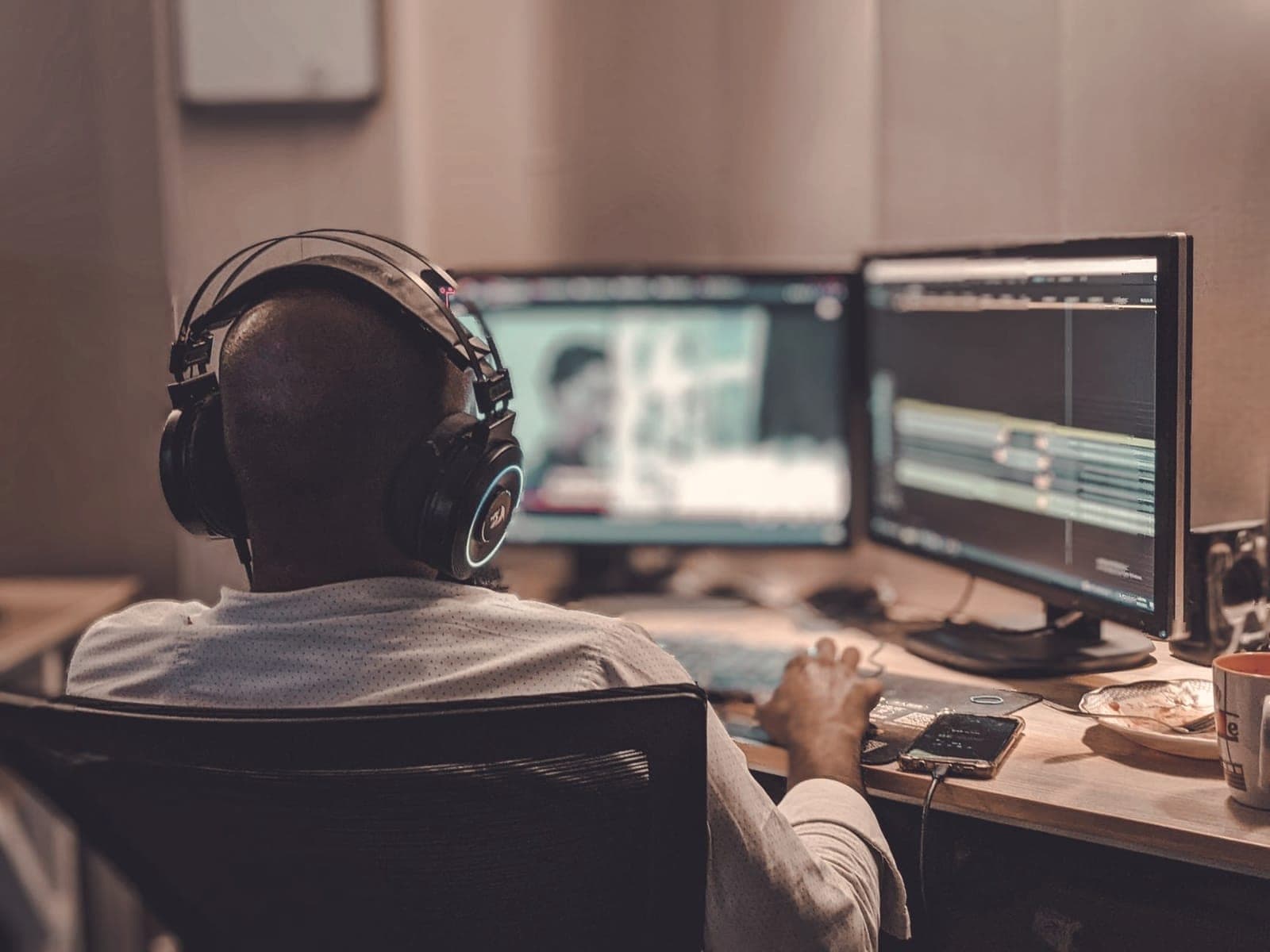 Video editor wearing headphones editing footage on dual monitors